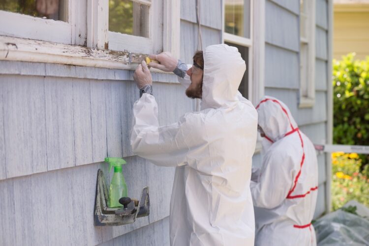 2 people in hazmat suits removing lead paint from the outside of a house